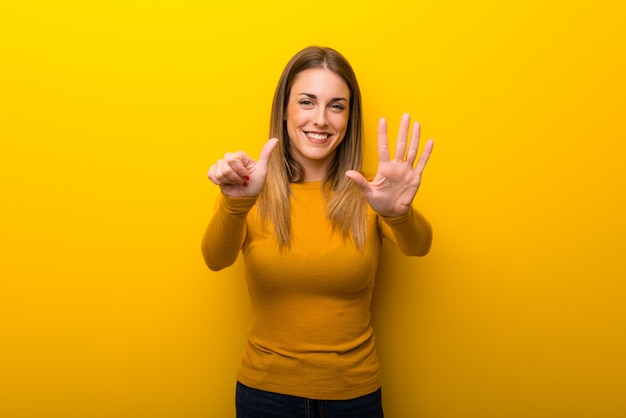 Junge Frau auf dem gelben Hintergrund, der sechs mit den Fingern zählt