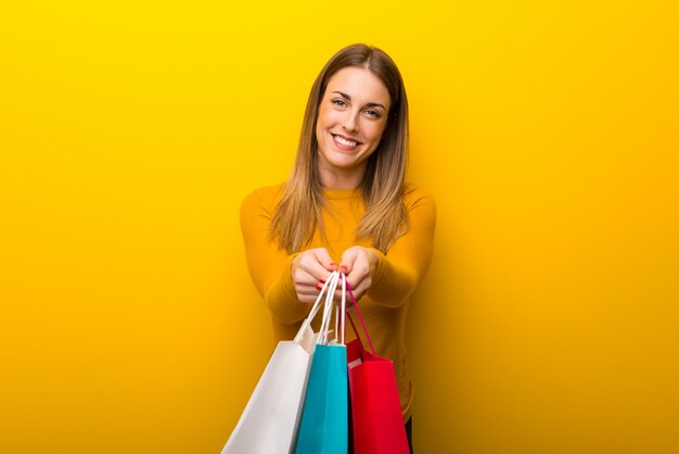 Junge Frau auf dem gelben Hintergrund, der viele Einkaufstaschen hält
