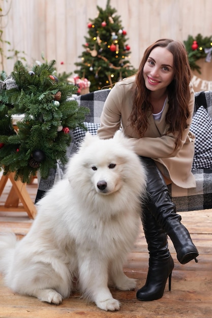 Junge Frau auf dem Hintergrund des Weihnachtsbaums mit weißem Samoyed-Hund im Freien Hofdekoration für das neue Jahr