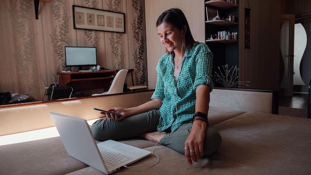 Foto junge frau auf dem sofa, die glücklich an einem neuen projekt mit laptop zu hause arbeitet