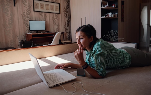 Junge Frau auf dem Sofa, die glücklich an einem neuen Projekt mit Laptop zu Hause arbeitet