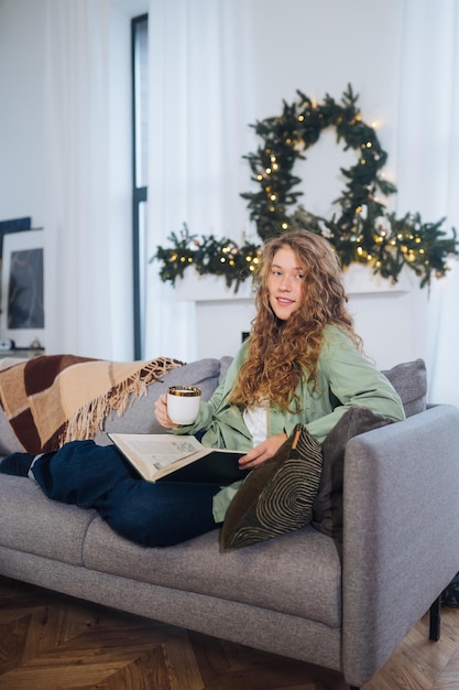 Junge frau auf der couch liest ein buch und genießt kaffee