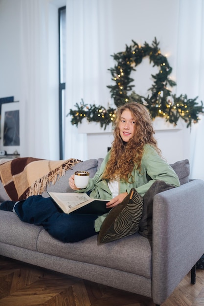 Junge Frau auf der Couch liest ein Buch und genießt Kaffee