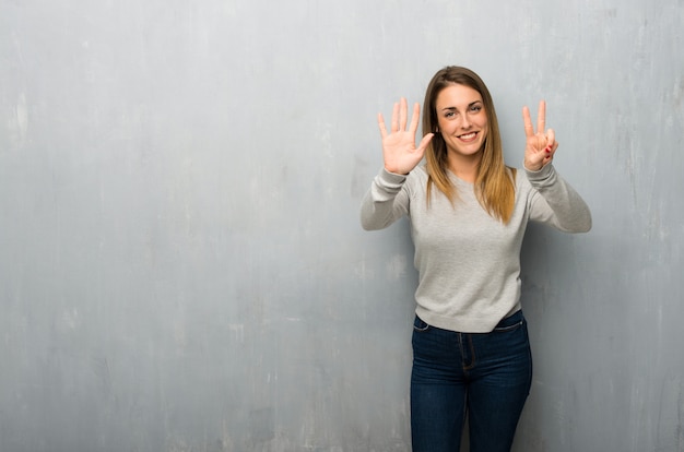 Junge Frau auf der strukturierten Wand, die sieben mit den Fingern zählt