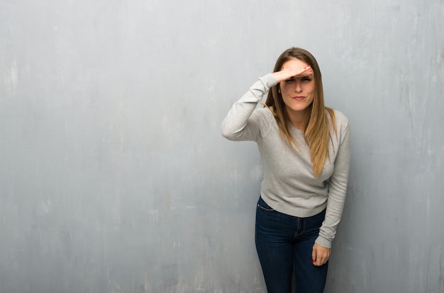 Junge Frau auf der strukturierten Wand, die weit mit der Hand schaut, um etwas zu schauen