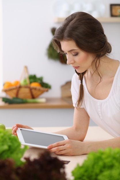 Junge Frau auf der Suche nach einem neuen Rezept zum Kochen in einer Küche. Hausfrau macht Online-Shopping per Tablet-Computer und Kreditkarte.