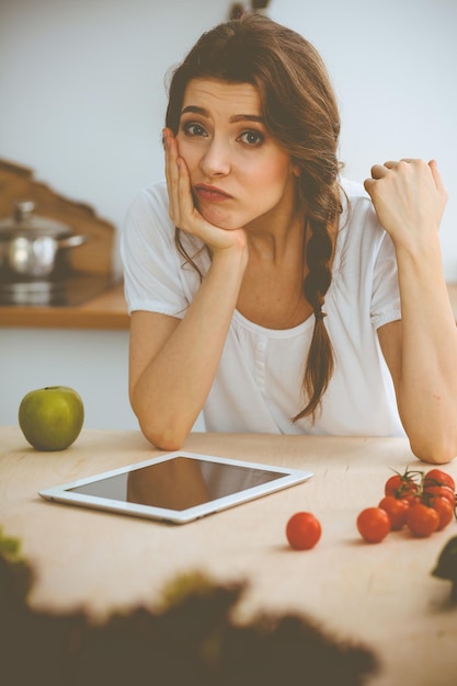 Junge Frau auf der Suche nach einem neuen Rezept zum Kochen in einer Küche. Hausfrau macht Online-Shopping per Tablet-Computer und Kreditkarte.