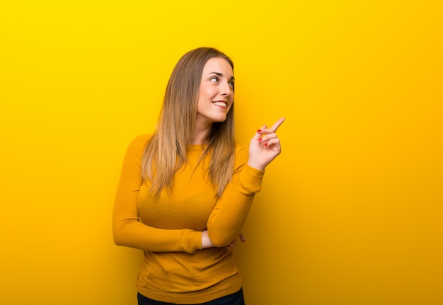 Junge Frau auf Gelb eine großartige Idee zeigend und oben schauend