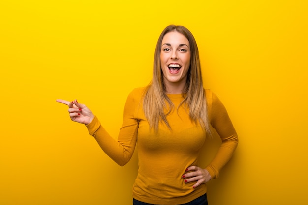 Junge Frau auf gelbem Hintergrund Finger auf die Seite zeigend und ein Produkt darstellend