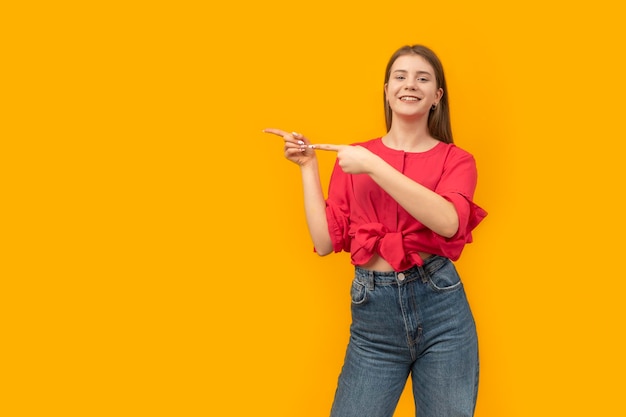 Junge Frau auf isoliertem orangefarbenem Hintergrund, die mit dem Finger zur Seite zeigt und lächelt Platz für Ihren Text