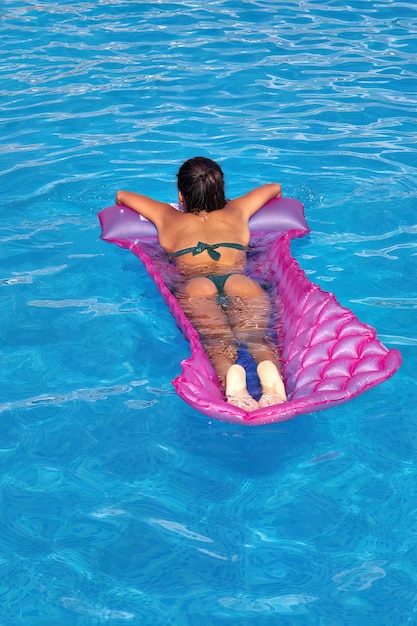 Junge Frau auf Matratze in einem Swimmingpool mit blauem Wasser