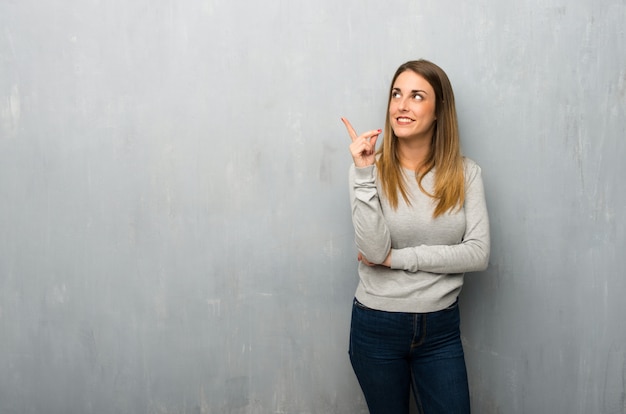 Junge Frau auf strukturierter Wand eine großartige Idee zeigend und oben schauend