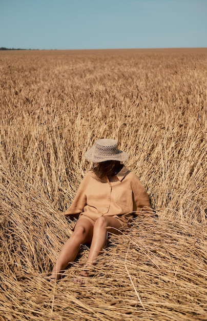 Junge Frau barfuß in Leinenkleidung und einem Hut auf einem Hintergrund von trockenem Gras romantisches Mädchen in einem Hut