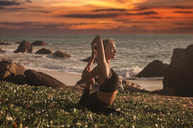 Junge Frau bei Sonnenuntergang macht Yoga für einen gesunden Lebensstil am tropischen Meer- oder Ozeanstrand im Freien