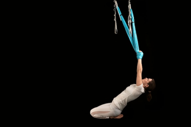 Junge Frau beim Aero-Fitness-Gymnastik-Stretching Aerial Fly Yoga und Stretching in Hängematten isoliert auf schwarzem Hintergrund