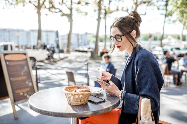 Junge Frau beim Frühstück mit Kaffee und Croissant im Freien im französischen Café in Lyon sitzend