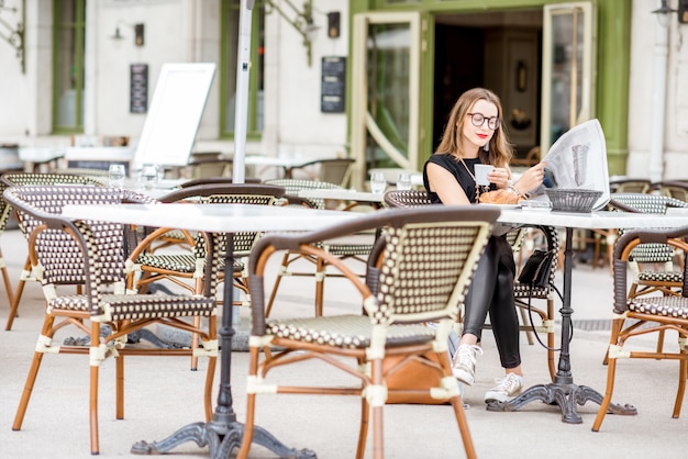 Junge Frau beim Frühstück mit Kaffee und Croissant Zeitung lesen im Freien auf der typisch französischen Café-Terrasse in Frankreich