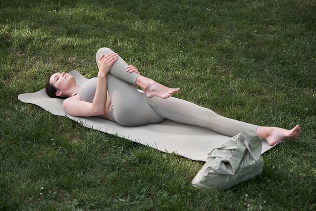 Junge Frau beim Yoga auf einer Matte im Park liegend