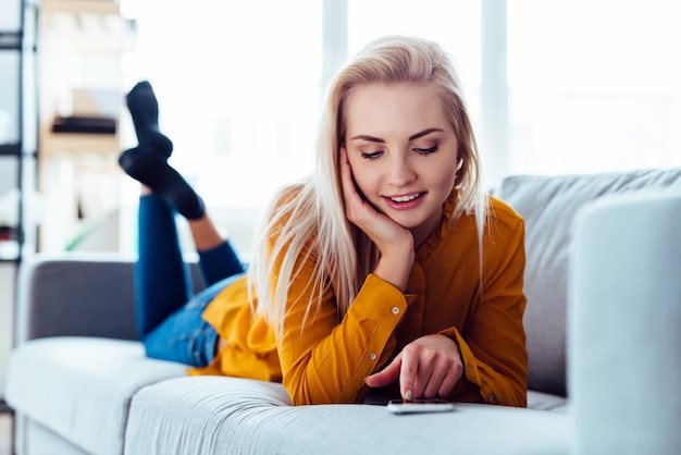 Junge Frau benutzt das Telefon, während sie auf dem Sofa liegt