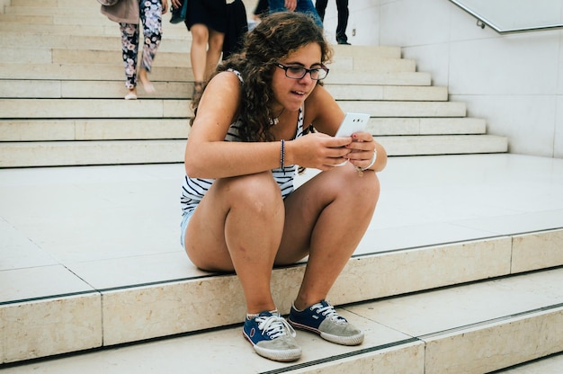 Foto junge frau benutzt das telefon, während sie auf der treppe sitzt