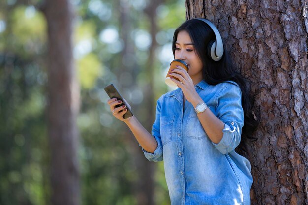 Junge Frau benutzt das Telefon, während sie auf einem Baumstamm steht