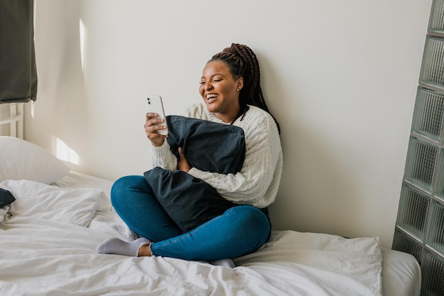 Junge Frau benutzt ein Handy, während sie zu Hause auf dem Bett liegt