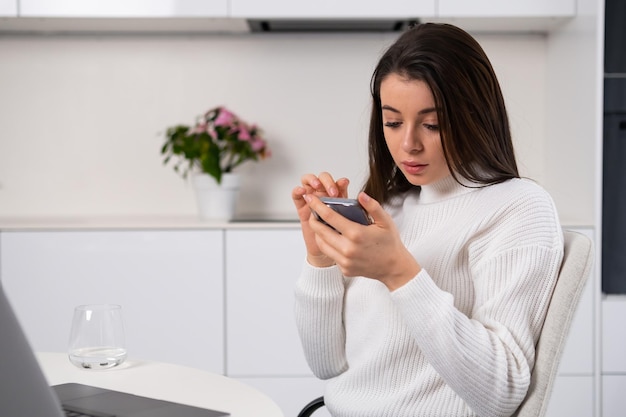 Junge Frau blickt in der Küche auf den Bildschirm ihres Smartphones