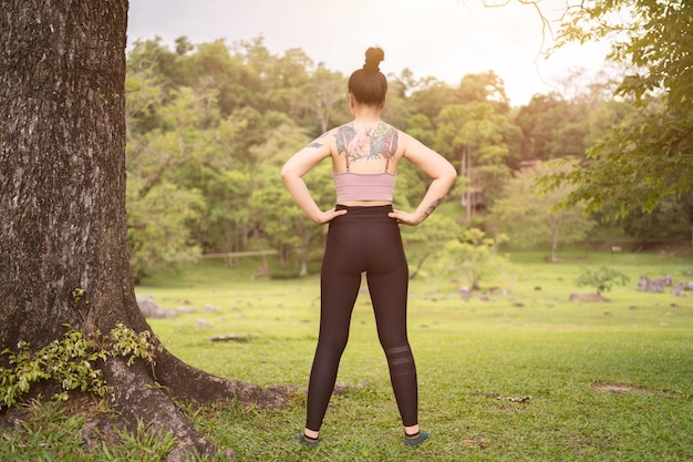 Junge Frau der asiatischen Tätowierung, die Yoga im Park tut