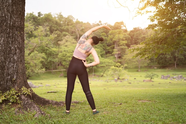 Junge Frau der asiatischen Tätowierung, die Yoga im Park tut