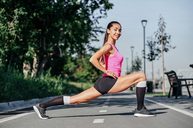 Junge Frau der Eignung, die Beine nach Laufsportporträt im Freien ausdehnt