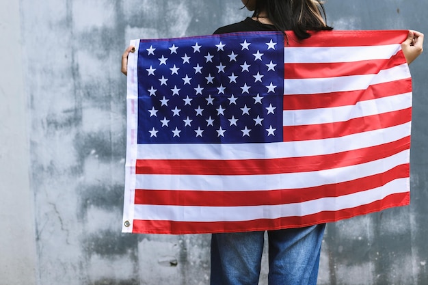 Junge Frau der hinteren Ansicht steht und hält eine amerikanische Flagge.