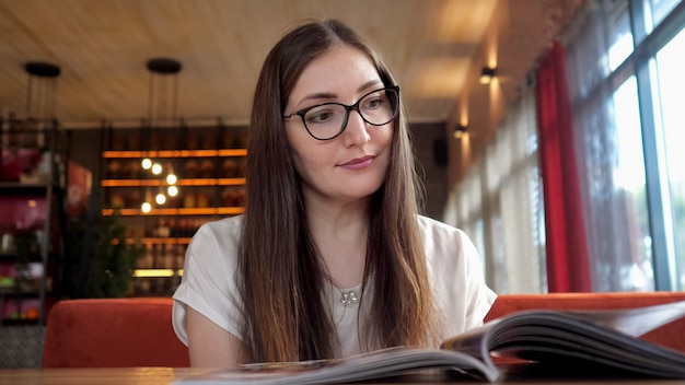 Junge Frau der Schönheit in den Gläsern, die Menü lesen. Lächelndes schönes Mädchen, das Essen im Café wählt.