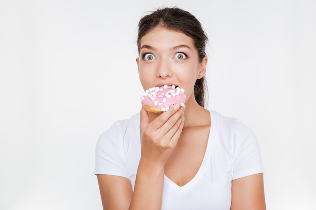 Junge Frau der verwirrten Diät, die leckeren Donut lokalisiert über weißer Wand isst