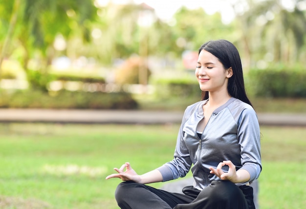 Junge Frau der Yogafrau, die Yoga tut und entspannen sich Meditation auf grüner Wiese im Park im Freien