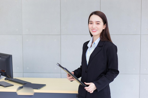 Junge Frau des asiatischen Berufsgeschäfts lächelt mit Selbstvertrauen, arbeitet und hält Klemmbrett im Büro