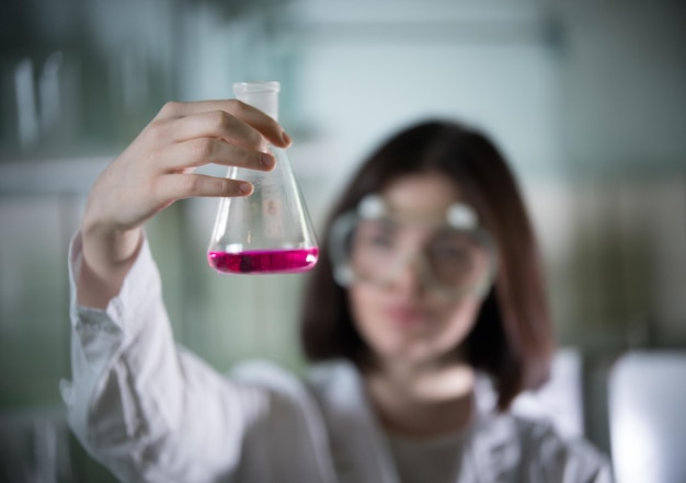 Junge Frau des chemischen Labors, die eine Flasche mit rosa Flüssigkeit darin hält Flasche im Fokus