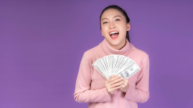 Junge Frau des erfolgreichen schönen asiatischen Geschäfts, die Geld US-Dollarscheine in der Hand hält, lokalisiert auf purpurrotem Hintergrund mit Kopienraumgeschäftskonzept