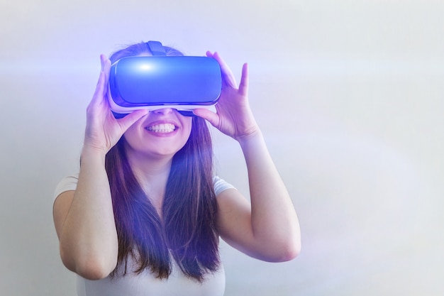 Junge Frau des Lächelns, die unter Verwendung des Glassturzhelmkopfhörers der virtuellen Realität VR auf Weiß trägt