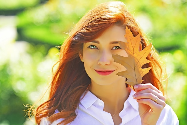 Junge Frau des Modeherbstes hält gelbe Ahornblätter auf Fallparkhintergrund.