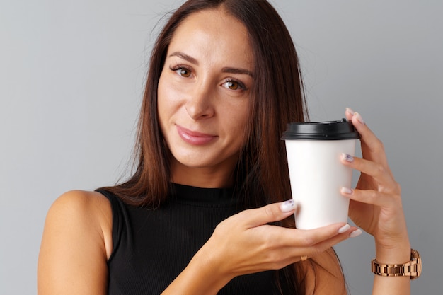 Junge Frau des netten Brunette, die einen Tasse Kaffee über einem grauen Hintergrund hält