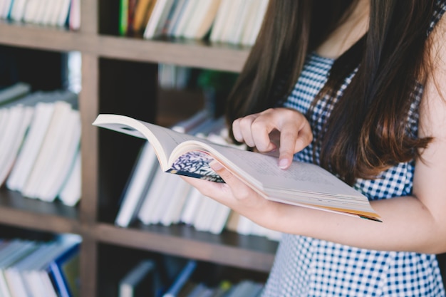 Junge Frau des schönen Mädchens, die gegen Bücherregal am Bibliotheksraum steht und sich lehnt