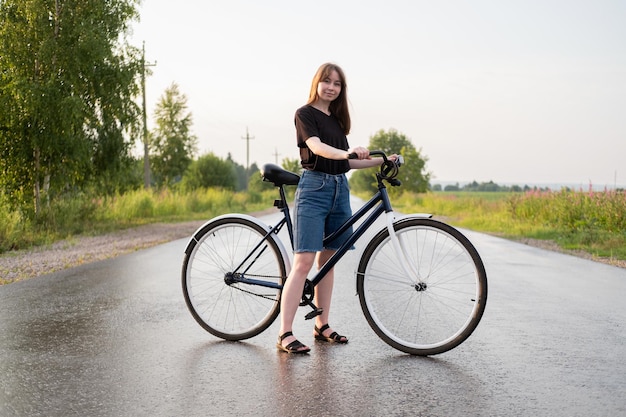 Junge Frau, die allein auf der Straße mit dem Fahrrad auf dem Land steht