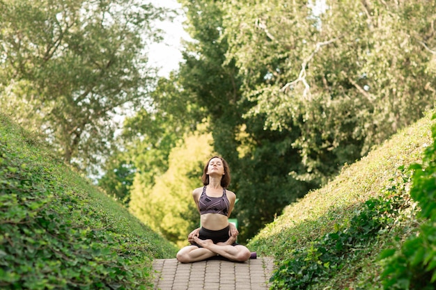 Junge Frau, die allein Yoga auf einer Parkgasse an einem sonnigen Sommertag tut.