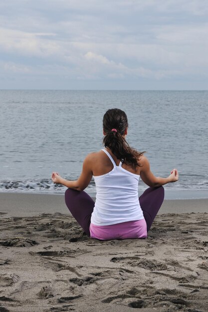 junge Frau, die am frühen Morgen Yoga in Lotusposition am Strand meditiert