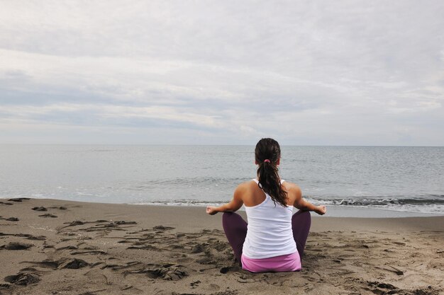 junge Frau, die am frühen Morgen Yoga in Lotusposition am Strand meditiert