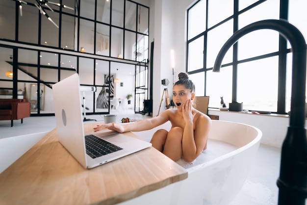 Junge Frau, die am Laptop arbeitet, während sie eine Badewanne nimmt