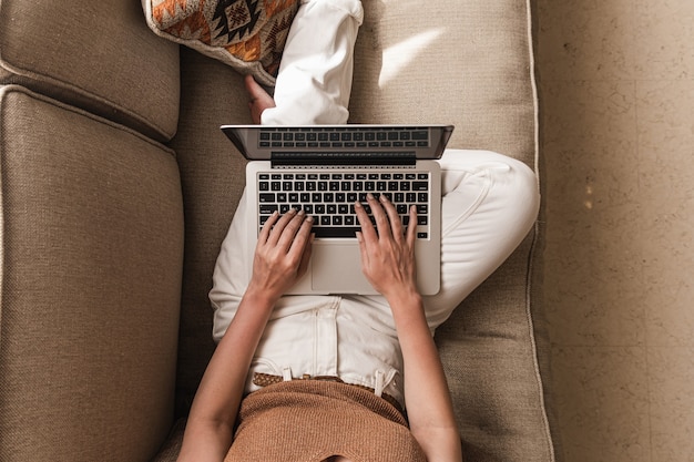 Junge Frau, die an einem Laptop arbeitet, der auf der Couch liegt