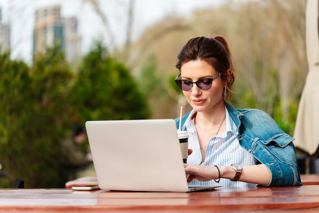 Junge Frau, die an einem Laptop in einem Café auf einer Außenveranda arbeitet