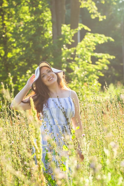 Junge Frau, die an einem sonnigen Sommertag zwischen Wildblumen spaziert. Konzept der Freude an der Kommunikation mit der Sommernatur