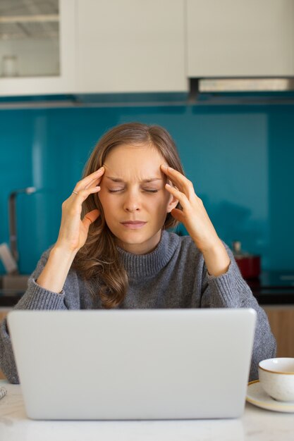 Junge Frau, die an Laptop arbeitet und stark denkt